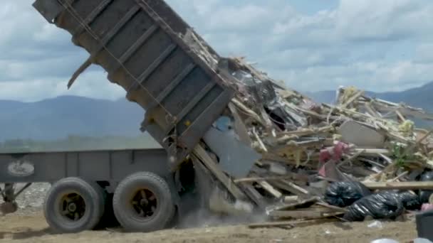 Мусоровоз опорожняет мусорный бак, заполненный строительными отходами, на свалке — стоковое видео