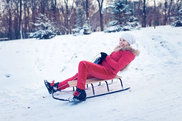 Усміхнена дівчина на санях у снігу взимку — стокове фото
