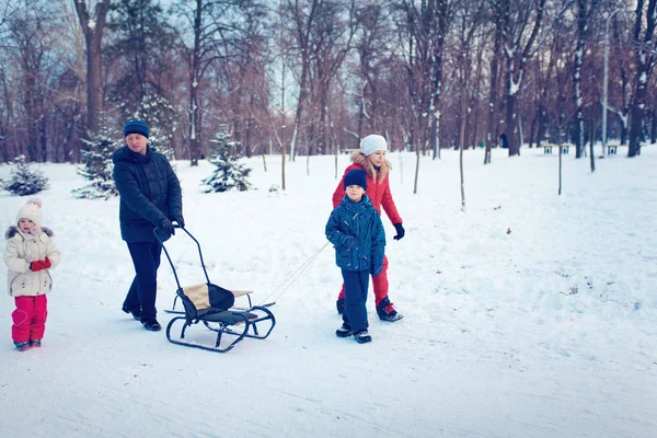 Jovem família correndo através da neve com trenó — Fotografia de Stock