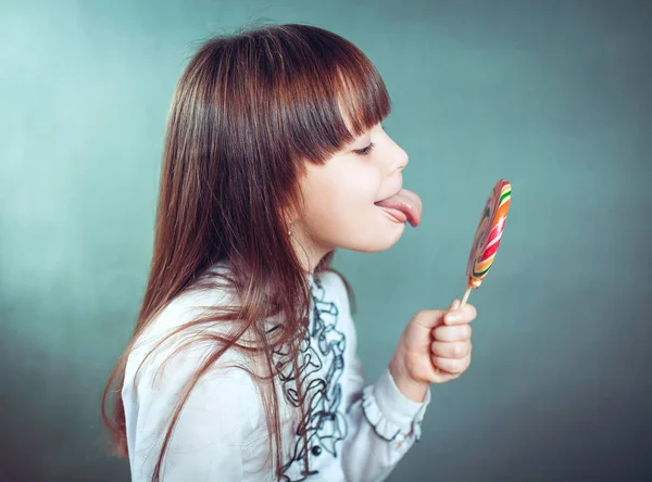 Vrolijke mooi meisje houdt dat een snoep knipoogt lacht toont taal — Stockfoto