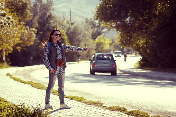 Young woman hitch-hiking on a road at the fields — Stock Photo, Image