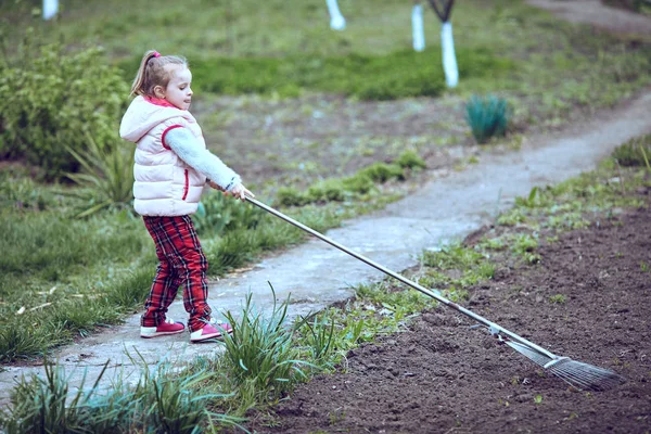 Kratta i trädgården. Ung flicka spela med rake. — Stockfoto