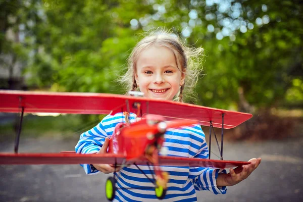 En flicka i en väst håller ett flygplan i sin hand — Stockfoto