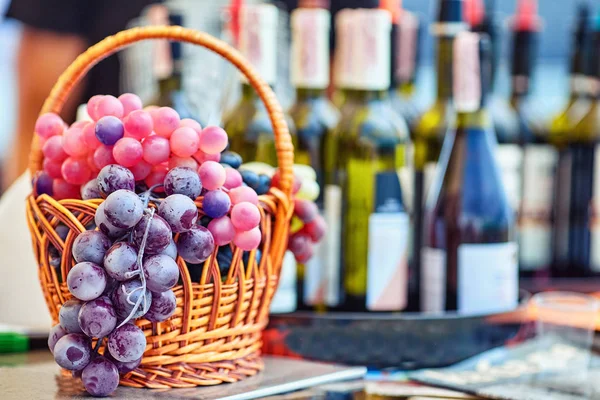 Uvas em uma cesta no fundo de garrafas de vinho — Fotografia de Stock