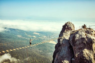 Kadın bir uçurumun üzerinde bir asma köprü yürüyor.