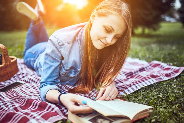 Девушка читает книгу в парке в летний закат молнии — стоковое фото