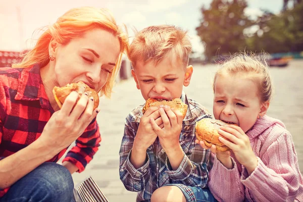 Anne ve çocuklar açık havada bir hamburger yemek