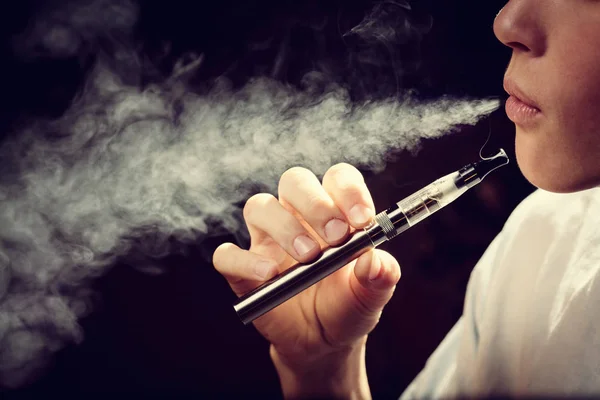 A young man blows smoke from an electronic cigarette — Stock Photo, Image