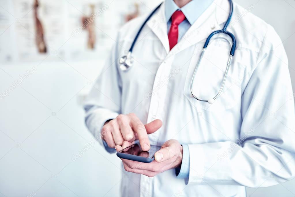 doctor in white medical coat  is using a smartphone and smiling 