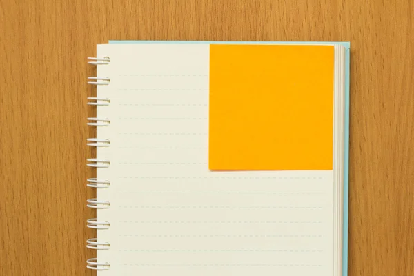 Open boek en oranje nota papier op houten tafel — Stockfoto