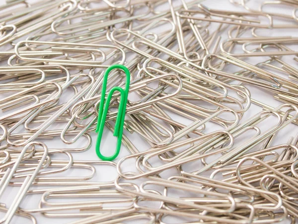 Green paper clip stand different from the crowd on white backgro