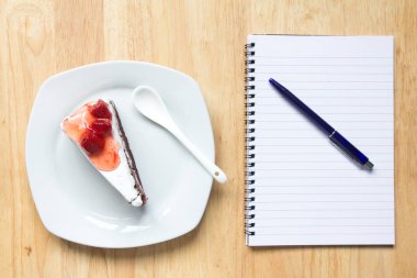 Çilekli pasta ve not defteri kalem ile ahşap arka plan üzerinde