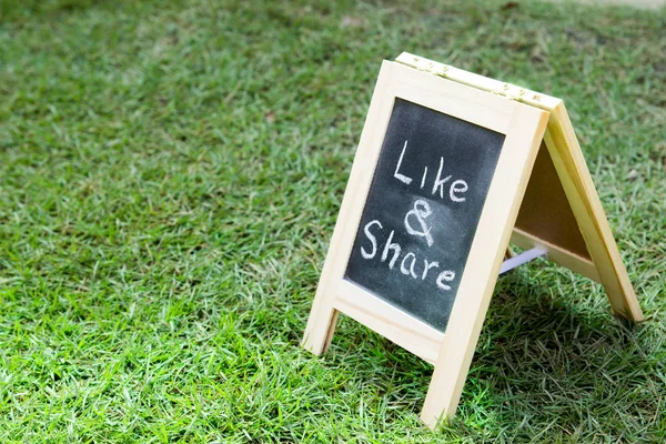 Blackboard with easel and wording like and share on green grass