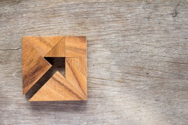 Tangram puzzle as arrow in square shape on wooden background (Cooncept for business direction and decision) clipart