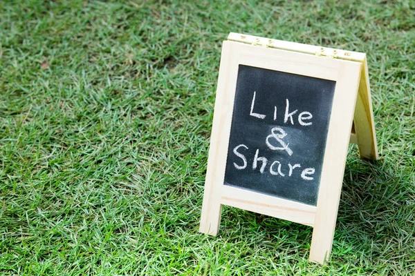 Blackboard with easel and wording like and share on green grass