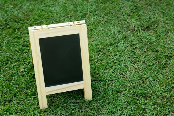 Tablero negro en blanco con caballete sobre fondo de hierba verde — Foto de Stock