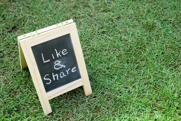 Blackboard with easel and wording like and share on green grass background