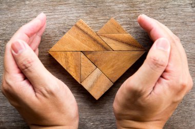 El kapak tangram bulmacanın ahşap arka plan üzerinde kalp şeklinde