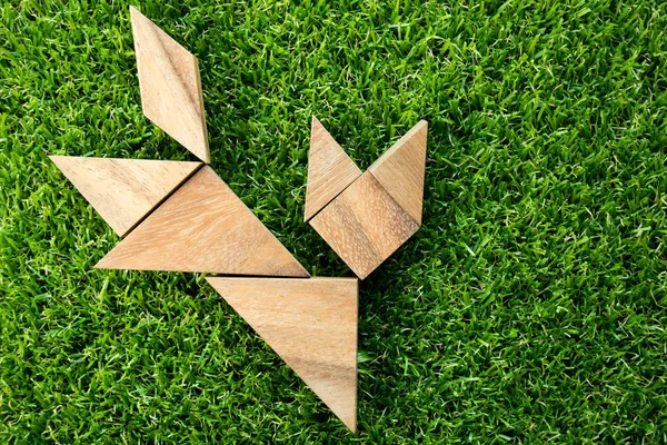 Wooden tangram puzzle in cat shape on artificial green grass background