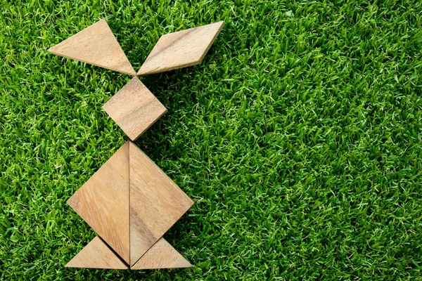 Wooden tangram puzzle in rabbit shape on artificial green grass background (Concept of Happy Easter)