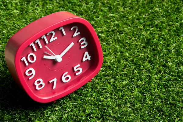 Red analog clock on artificial green grass background — Stock Photo, Image