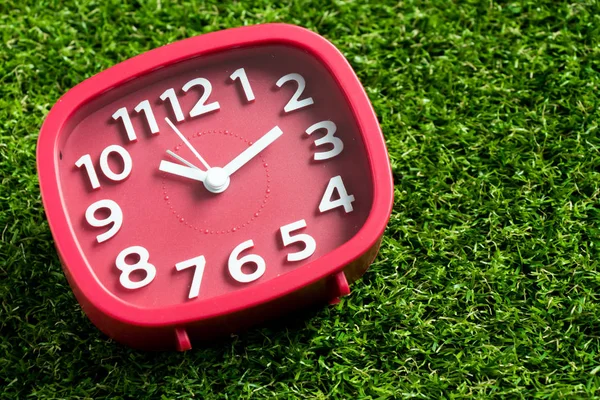 Czerwony zegar analogowy na tle Sztuczna trawa zielony — Zdjęcie stockowe