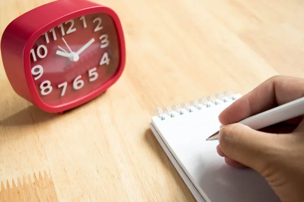 Man hold the pen with book and red clock on wooden table background — Stock Photo, Image