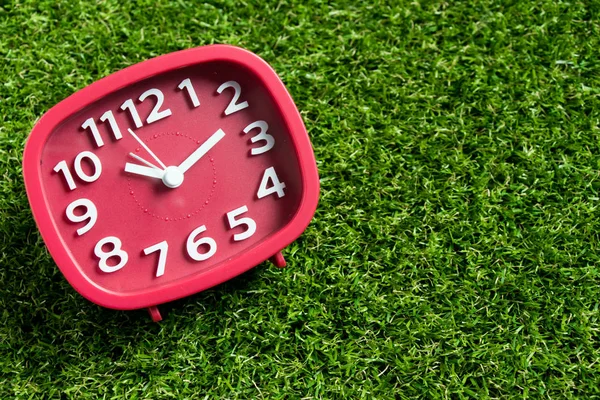 Red analog clock on artificial green grass background — Stock Photo, Image