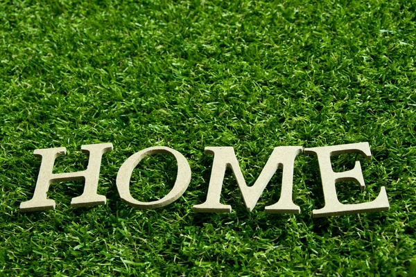 Wooden alphabet in wording home on artificial green grass background — Stock Photo, Image