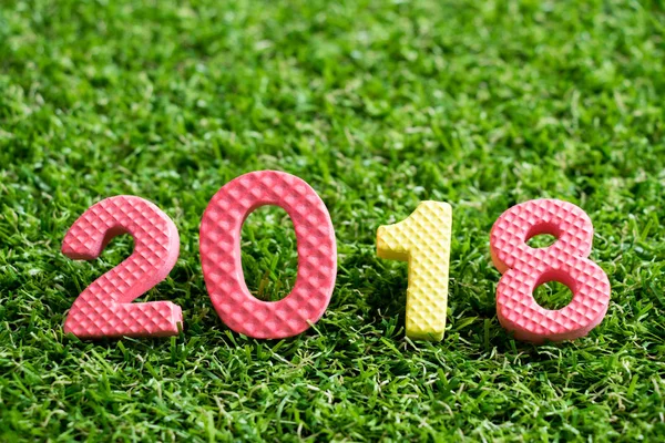 Oyuncak köpük alfabe arka planda ifade 2018 üzerinde yapay yeşil çim (Happy new year dekorasyon konsepti) — Stok fotoğraf