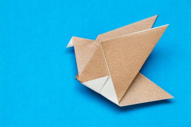 Kuş şekli mavi arka plan üzerinde uçan kahverengi origami kağıt