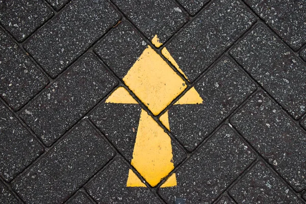 Yellow arrow paint on black brick concrete background