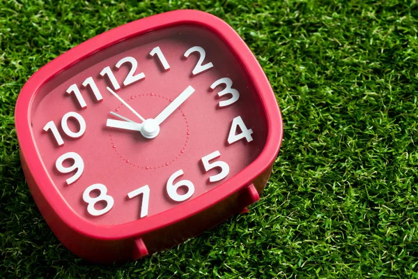 Red analog clock on artificial green grass background — Stock Photo, Image