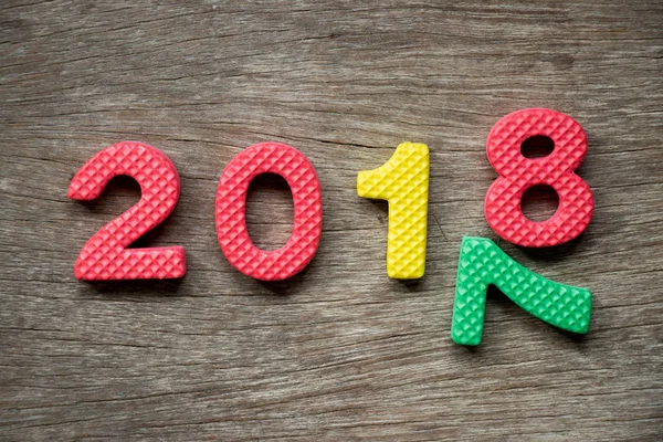 Toy foam alphabet in wording 2018 and falling number 7 on wood background (Concept for Happy new year) — Stock Photo, Image