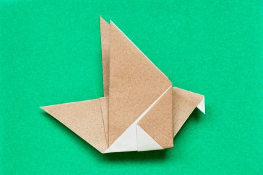 Kuş şekli yeşil arka plan üzerinde uçan kahverengi origami kağıt
