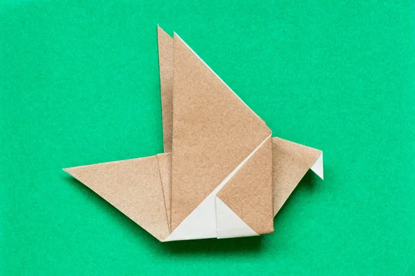 Kuş şekli yeşil arka plan üzerinde uçan kahverengi origami kağıt