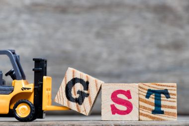 Sarı Plastik forklift ahşap arka plan üzerinde kelime Gst (kısaltma mal ve hizmet vergisi) tamamlamak için G harfi tutun