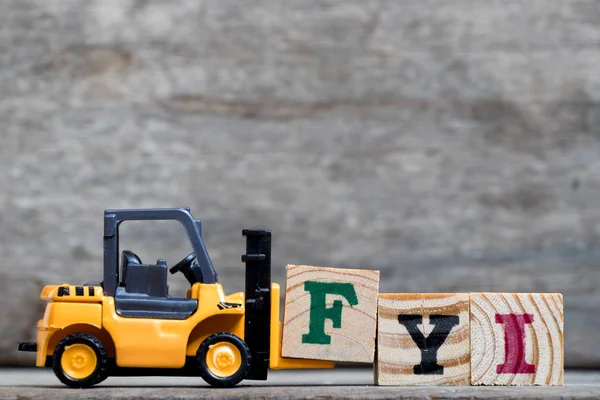 Gelber Kunststoff-Gabelstapler hält Buchstabe f, um das Wort fyi (Abkürzung für zu Ihrer Information) auf Holz-Hintergrund zu vervollständigen — Stockfoto