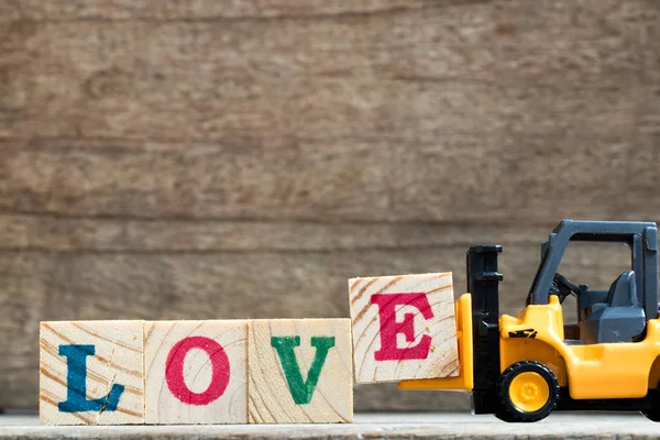 Toy plastic forklift hold block E to compose and fulfill wording love on wood background — Stock Photo, Image