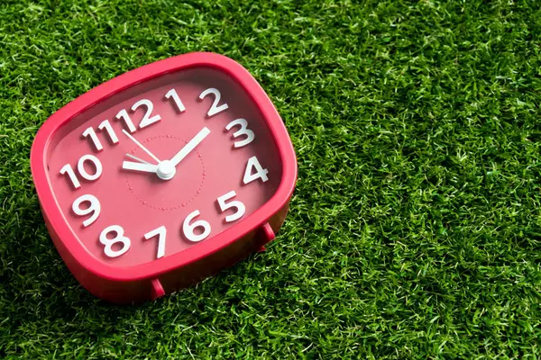 Red analog clock on artificial green grass background — Stock Photo, Image