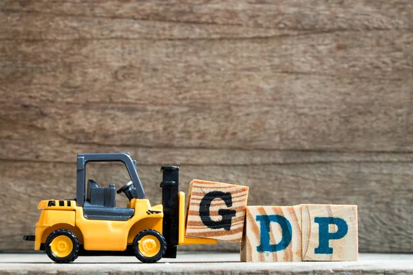Toy plastic forklift hold block G to compose and fulfill wording GDP (Gross domestic product or Good distribution practice) on wood background — Stock Photo, Image
