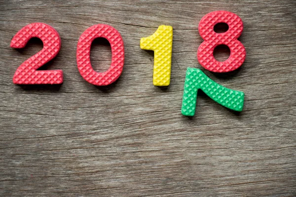 Spielzeugschaumstoff-Alphabet im Wortlaut 2018 und fallende Zahl 7 auf Holzgrund (Konzept für ein frohes neues Jahr)) — Stockfoto
