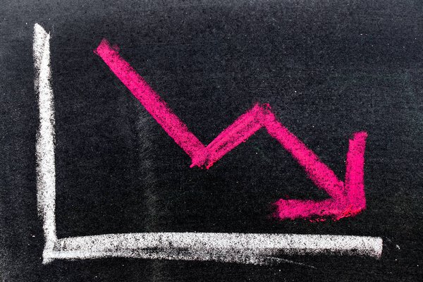 Red color hand drawing chalk in arrow down shape on black board background (Concept of stock decline, down trend of business, economy)