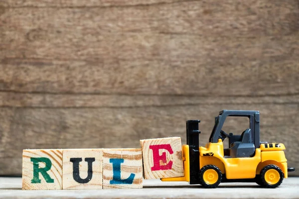 Empilhadeira de brinquedo de plástico amarelo segure o bloco de letra E para completar a regra da palavra no fundo de madeira — Fotografia de Stock