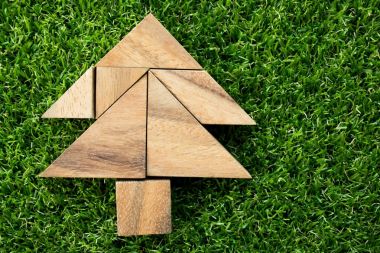 Wood tangram puzzle in Christmas tree shape on artificial green grass background clipart