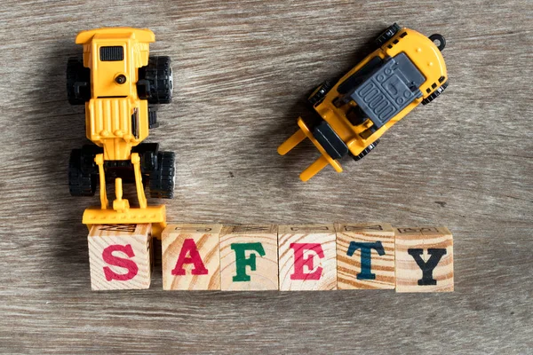 Zabawki z tworzyw sztucznych spychacz przytrzymaj toy block list s spełnić słowo bezpieczeństwa z wózka widłowego na tle drewna — Zdjęcie stockowe