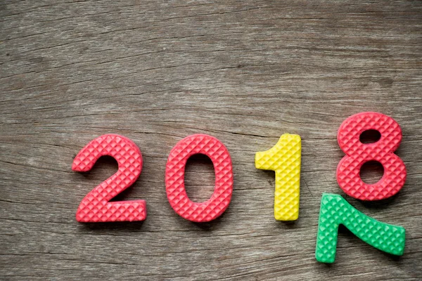 Spielzeugschaumstoff-Alphabet im Wortlaut 2018 und fallende Zahl 7 auf Holzgrund (Konzept für ein frohes neues Jahr)) — Stockfoto