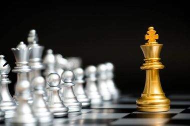 Satranç oyununda altın kral siyah zemin üzerinde başka bir gümüş takım ile karşı karşıya (Şirket stratejisi, iş zaferi veya karar kavramı)