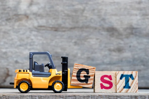 Sarı Plastik forklift ahşap arka plan üzerinde kelime Gst (kısaltma mal ve hizmet vergisi) tamamlamak için G harfi tutun