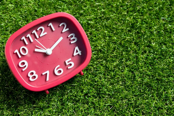 Red analog clock on artificial green grass background — Stock Photo, Image